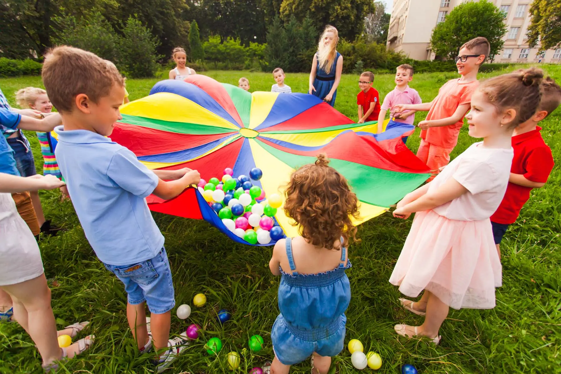 Close view kids having fun at summer birthday party. Games involving everyone. Activities for children of different age. Colorful parachute as game to unite and to teach cooperation