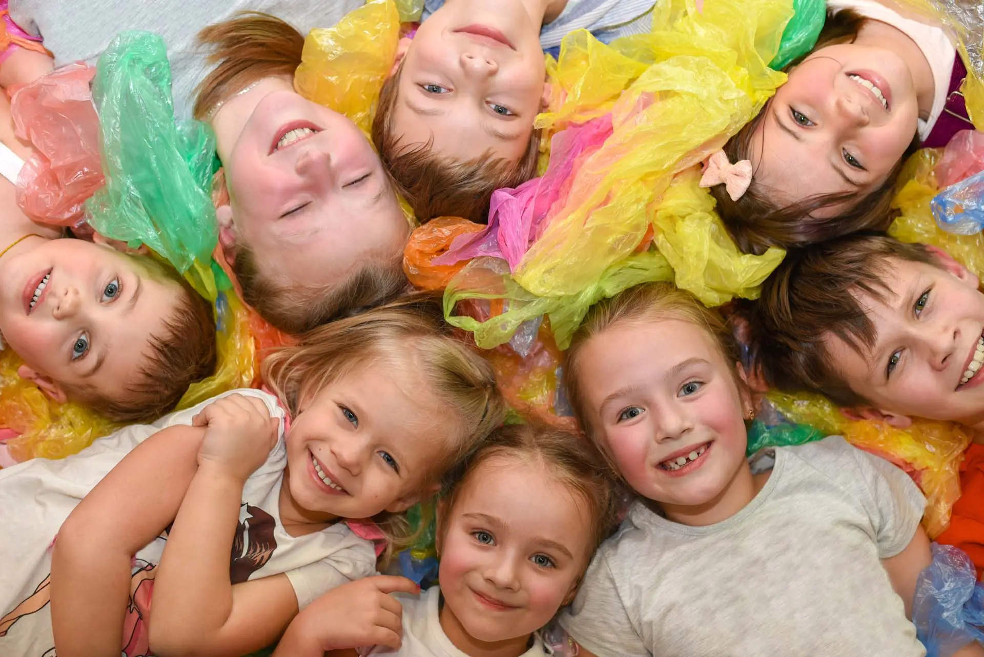 A group of children at a party lying on colored paper and laughing, top view.